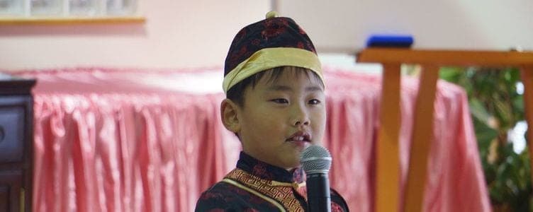 A student in a Chinese jacket and cap speaking into a microphone