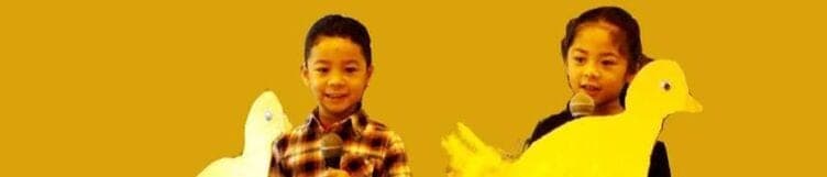 Two young students at microphones, holding paper duck cut-outs