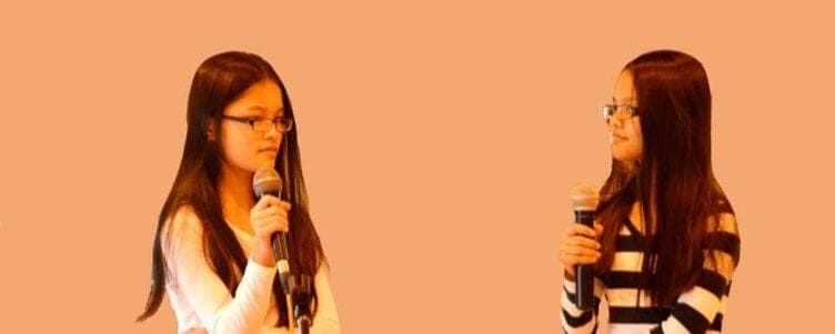 Two students speaking into microphones at a school ceremony