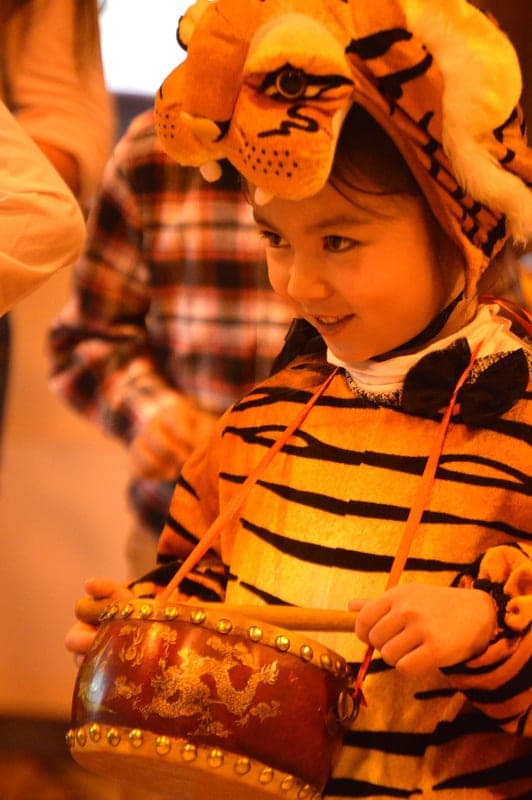 A student in a tiger costume playing a drum at a New Year celebration
